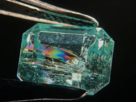 A rainbow flash is seen when viewing this fracture-filled emerald at the right angle, under darkfield illumination.