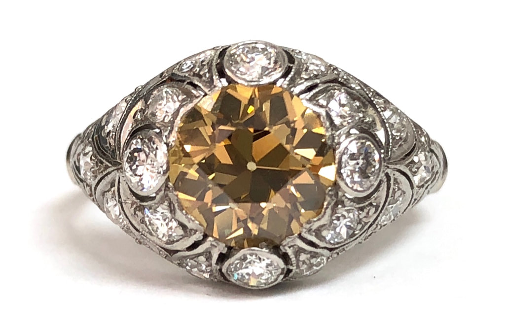 A fancy intense brownish yellow old European cut diamond is set at the center of this Art Deco era platinum filigree and diamond setting