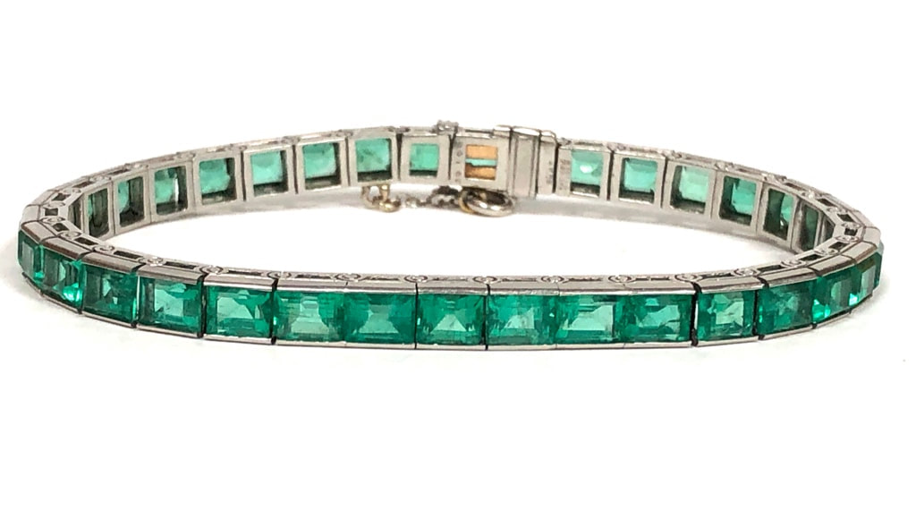 An Art Deco Era antique emerald and platinum line bracelet with wonderful hand chased gallery
